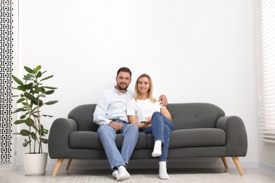 Photo of Couple with air conditioner remote control on sofa at home