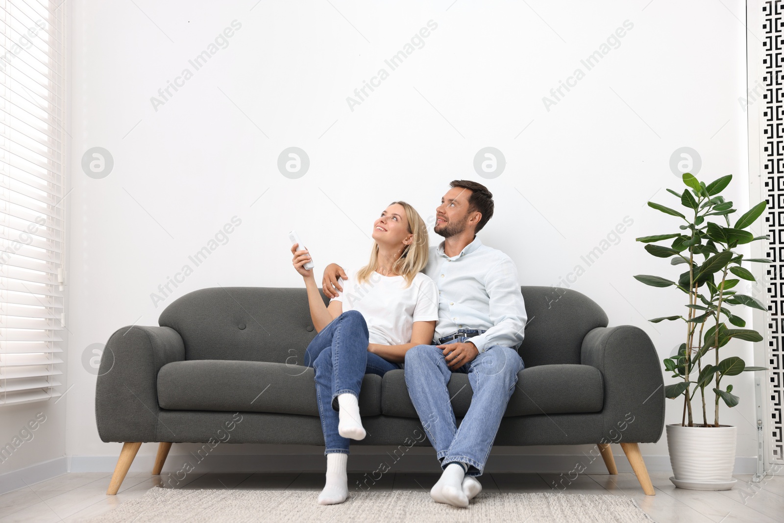 Photo of Couple using remote to control air conditioner on sofa at home
