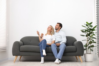 Photo of Couple using remote to control air conditioner on sofa at home