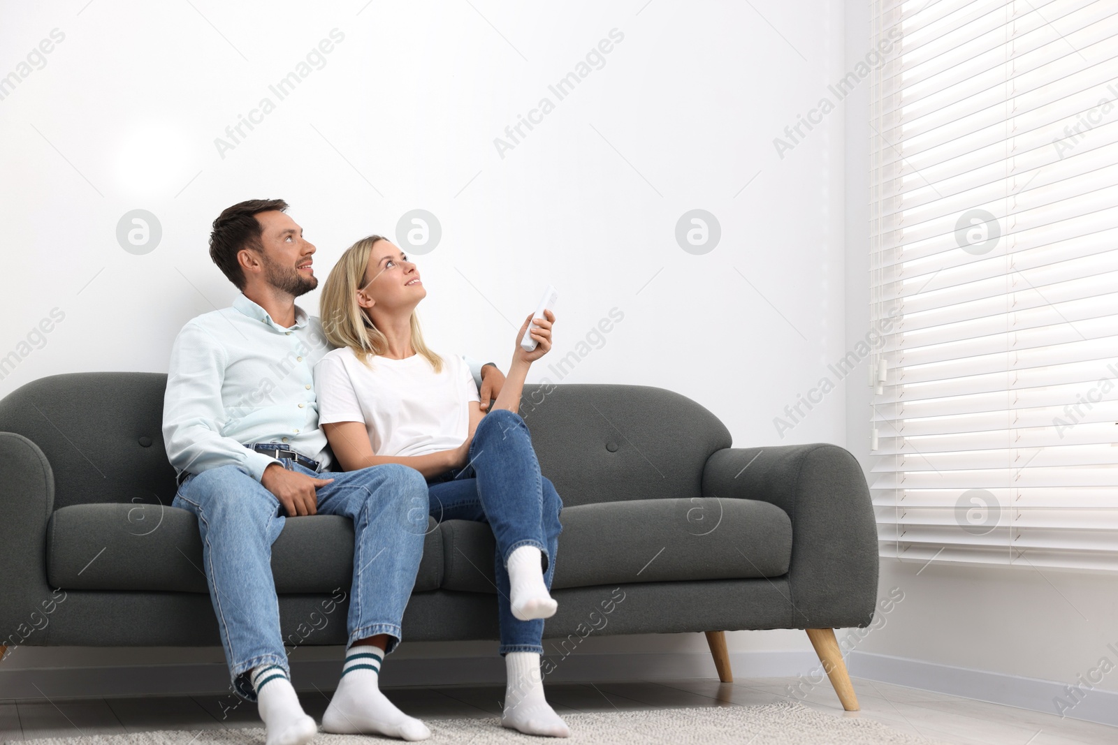Photo of Couple using remote to control air conditioner on sofa at home. Space for text