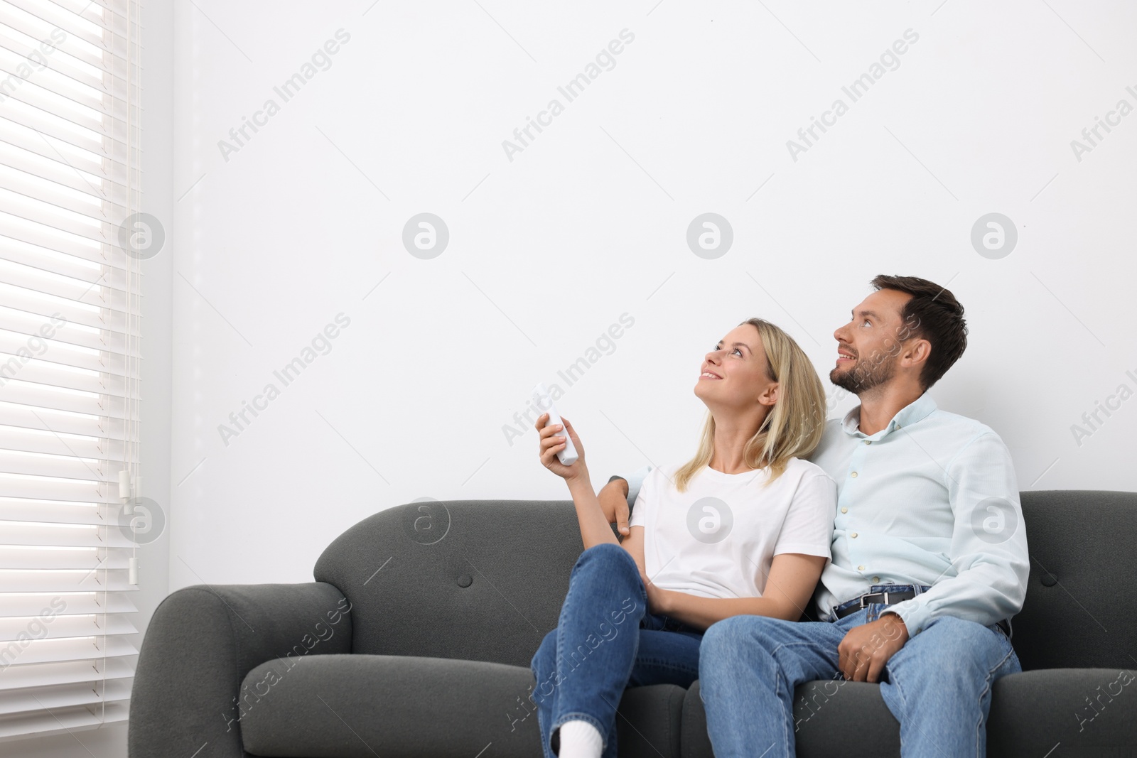 Photo of Couple using remote to control air conditioner on sofa at home. Space for text
