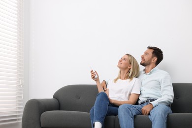 Photo of Couple using remote to control air conditioner on sofa at home. Space for text