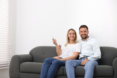 Photo of Couple using remote to control air conditioner on sofa at home. Space for text