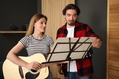 Photo of Tutor teaching woman to play guitar indoors