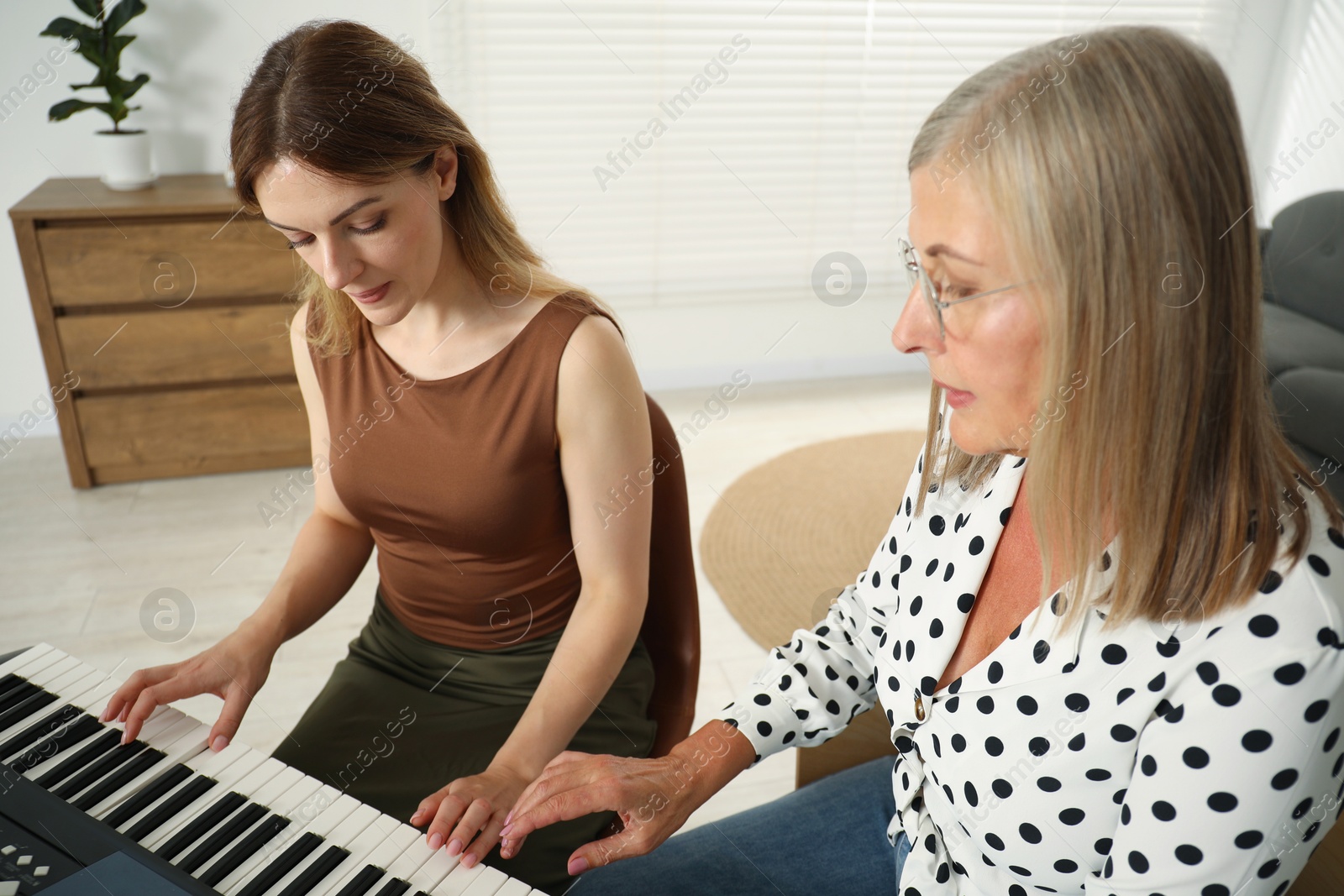 Photo of Tutor teaching woman to play piano indoors