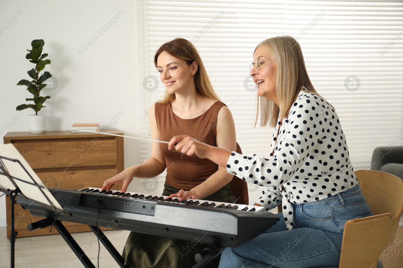 Photo of Tutor teaching woman to play piano indoors