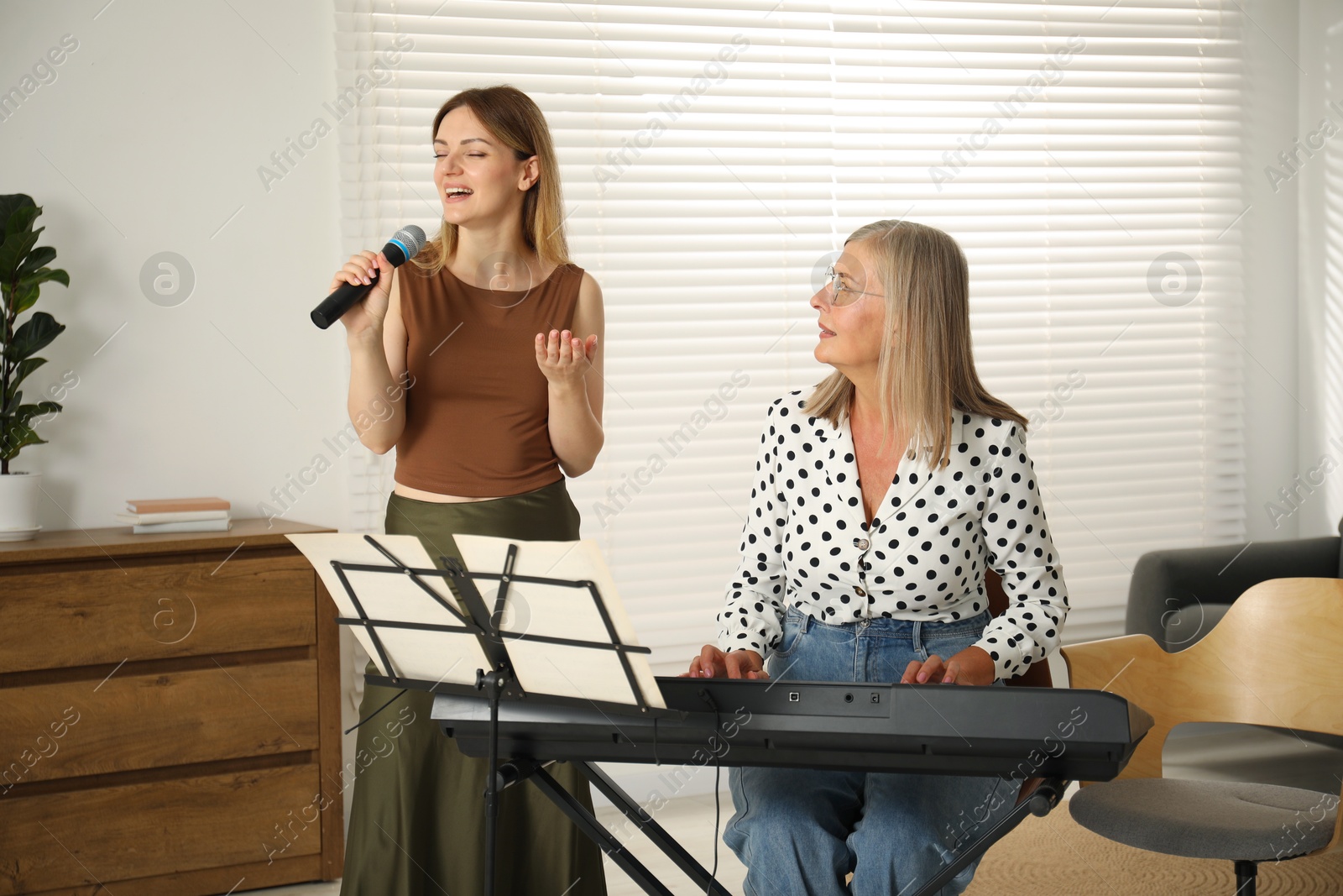 Photo of Woman learning to sing while her teacher accompanying on piano indoors