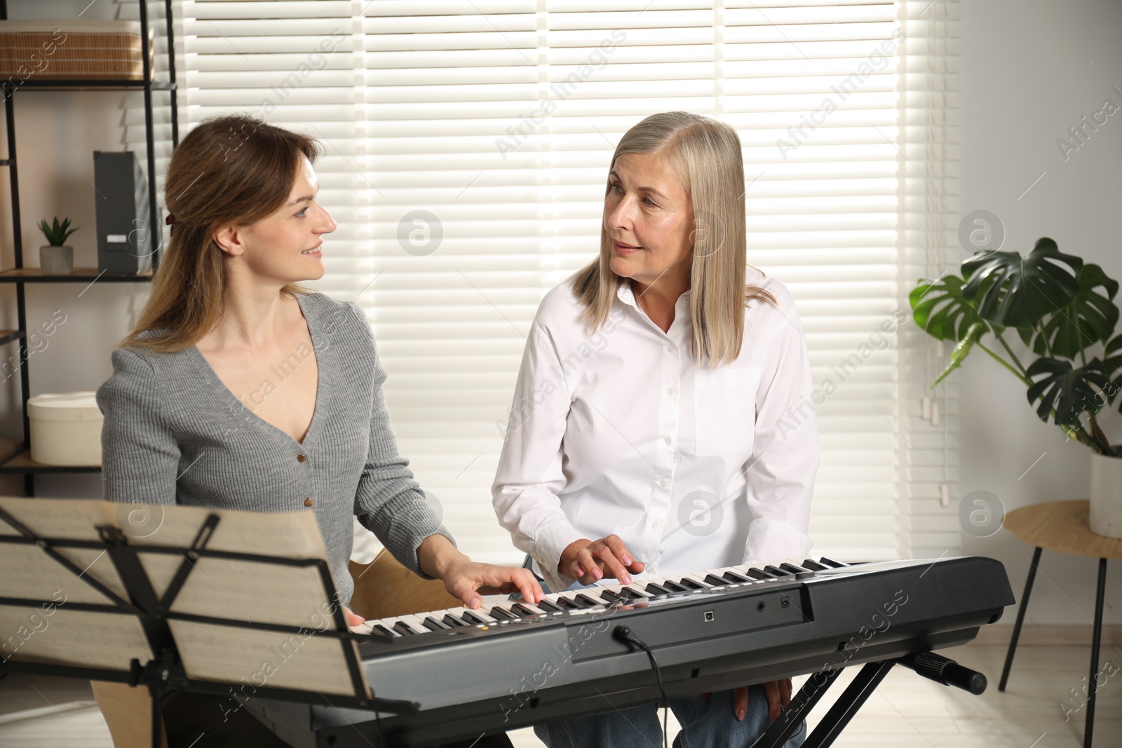 Photo of Tutor teaching woman to play piano indoors