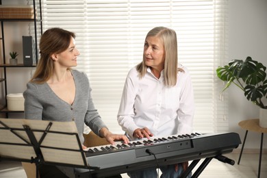 Photo of Tutor teaching woman to play piano indoors