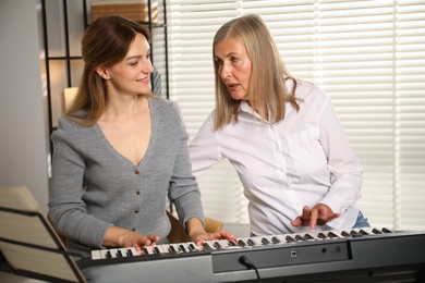 Photo of Tutor teaching woman to play piano indoors