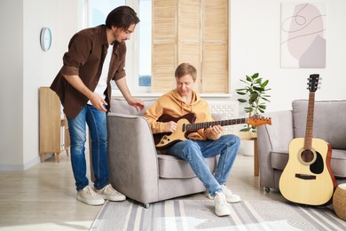 Photo of Tutor teaching man to play guitar at home