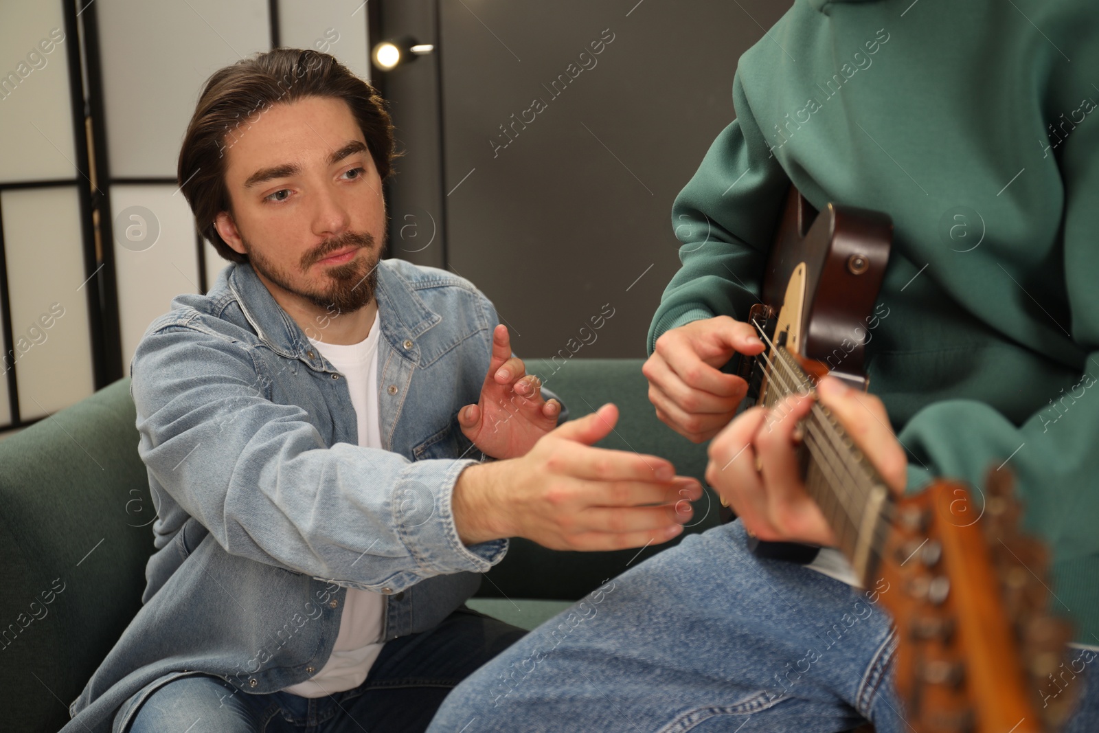 Photo of Tutor teaching man to play guitar at home, closeup
