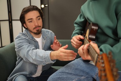 Photo of Tutor teaching man to play guitar at home, closeup