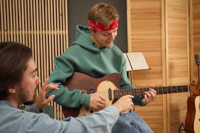 Photo of Tutor teaching man to play guitar indoors