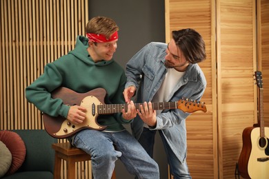 Photo of Tutor teaching man to play guitar indoors