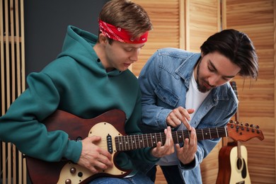 Photo of Tutor teaching man to play guitar indoors