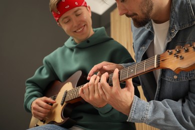 Photo of Tutor teaching man to play guitar at home, closeup