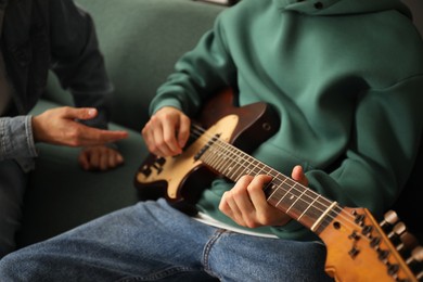 Photo of Tutor teaching man to play guitar at home, closeup