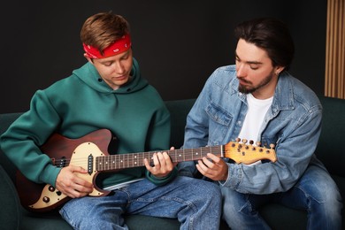 Photo of Tutor teaching man to play guitar on sofa indoors