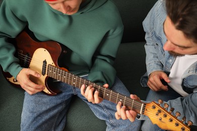 Photo of Tutor teaching man to play guitar at home, closeup
