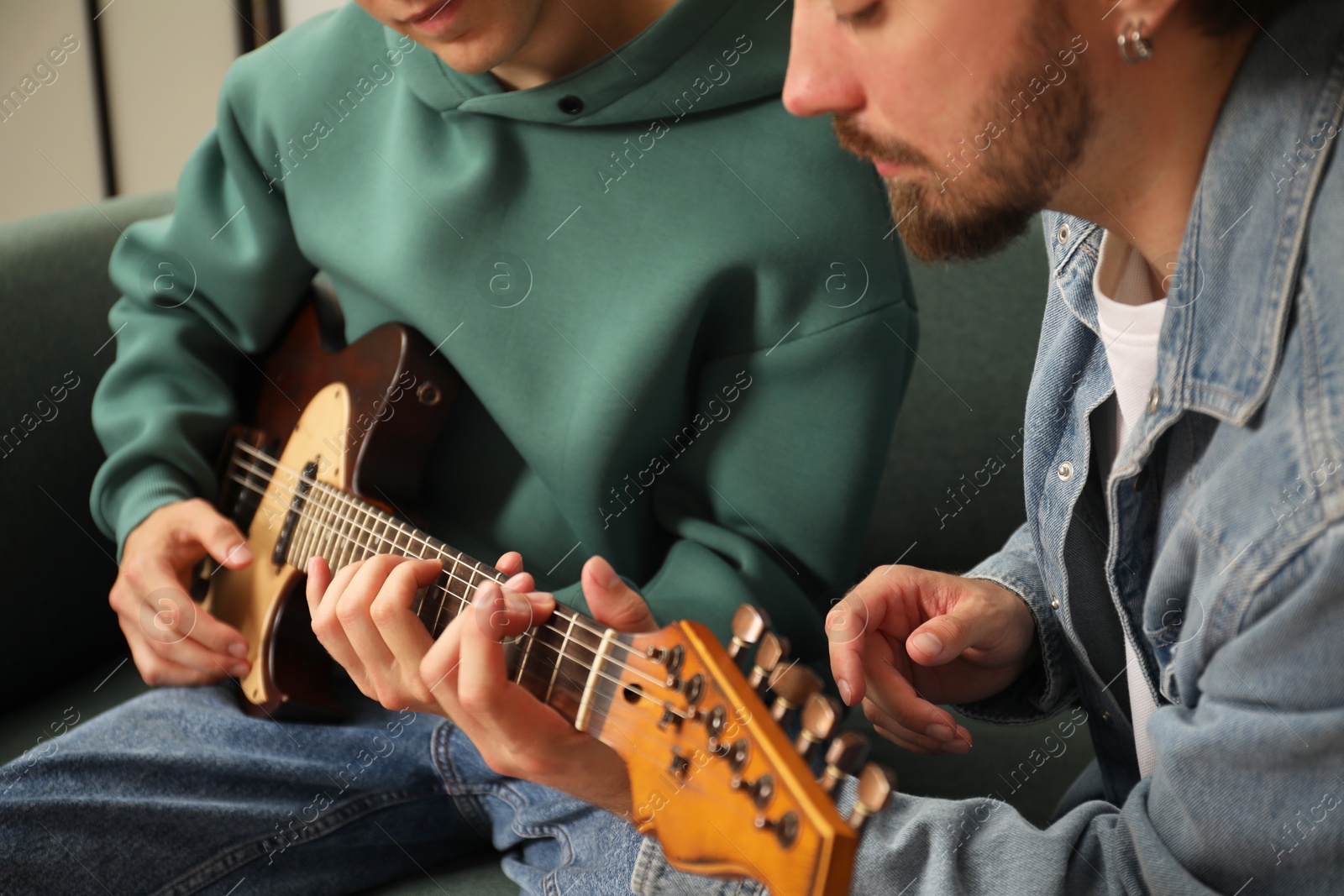 Photo of Tutor teaching man to play guitar at home, closeup