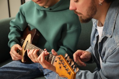 Photo of Tutor teaching man to play guitar at home, closeup