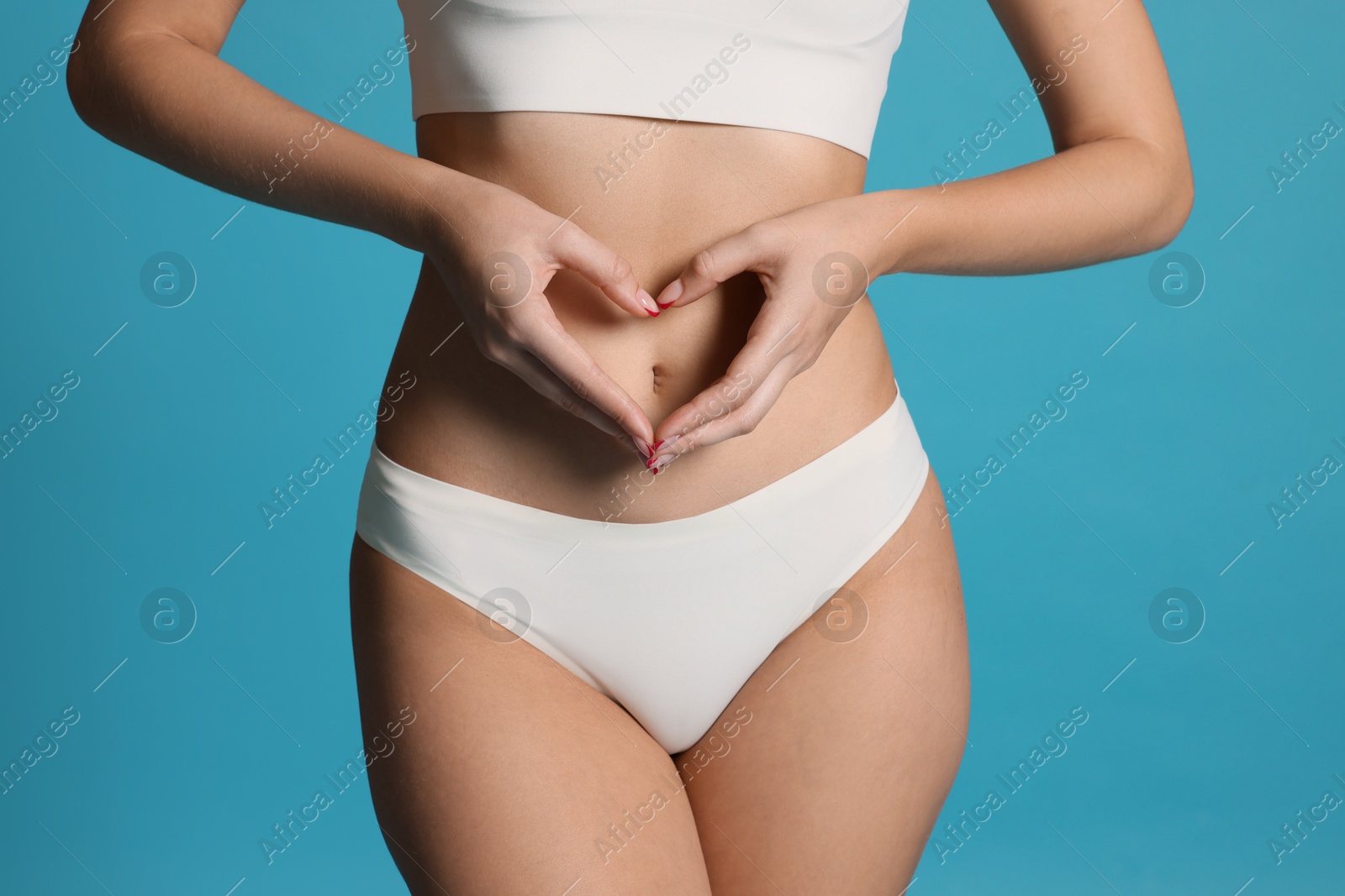 Young woman with flat belly making heart gesture on light blue background, closeup Photo of Young woman with flat belly making heart gesture on light blue background, closeup