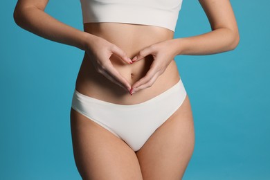 Photo of Young woman with flat belly making heart gesture on light blue background, closeup