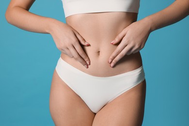 Photo of Young woman with flat belly on light blue background, closeup