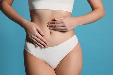 Photo of Young woman with flat belly on light blue background, closeup