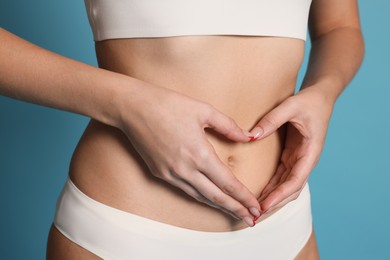 Photo of Young woman with flat belly making heart gesture on light blue background, closeup