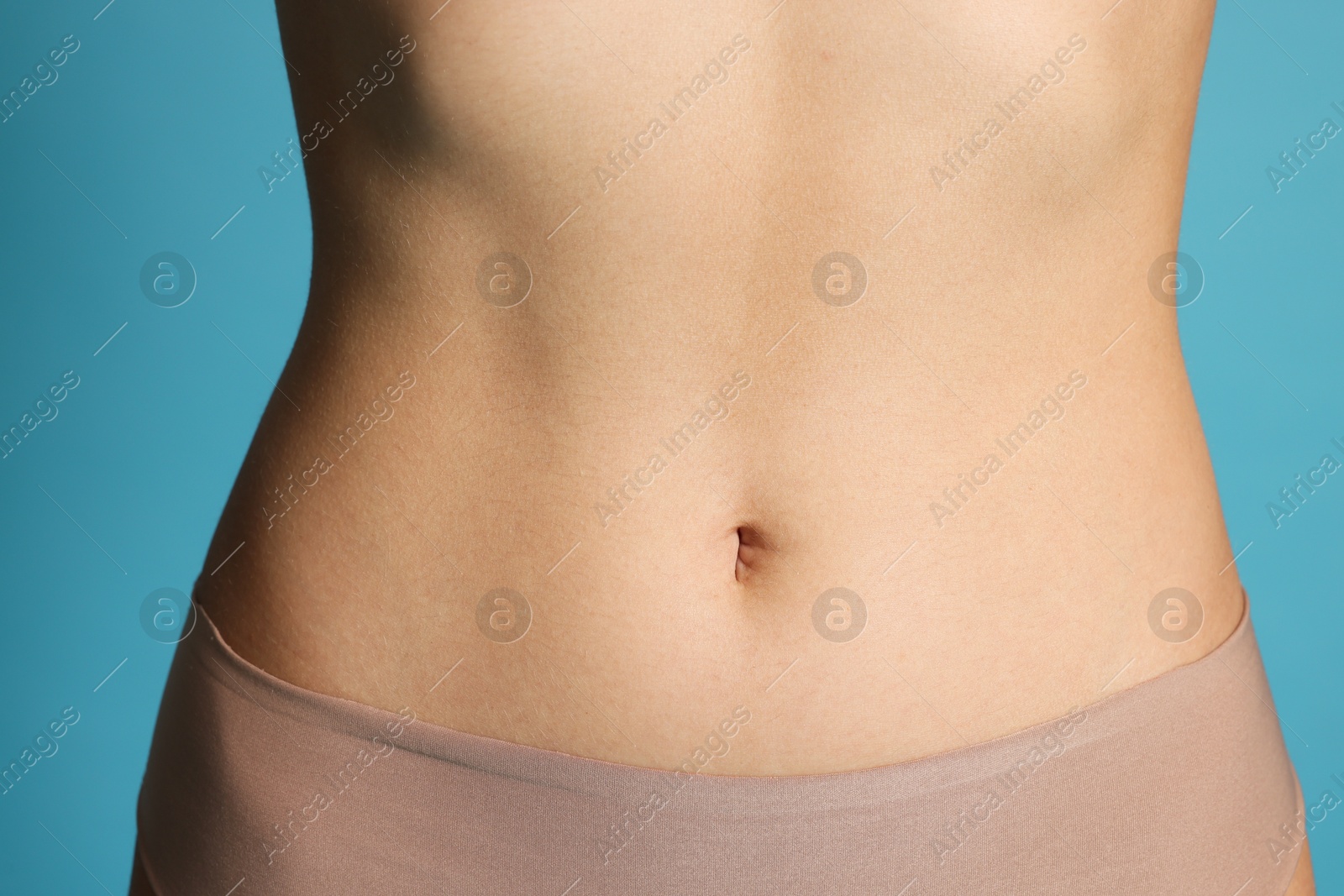 Photo of Young woman with flat belly on light blue background, closeup