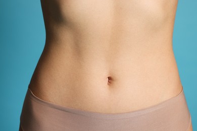 Photo of Young woman with flat belly on light blue background, closeup