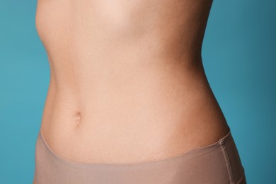 Photo of Young woman with flat belly on light blue background, closeup