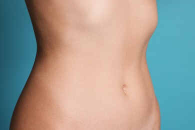 Photo of Young woman with flat belly on light blue background, closeup