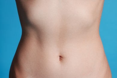Photo of Young woman with flat belly on light blue background, closeup