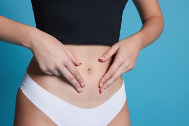 Photo of Young woman with flat belly on light blue background, closeup