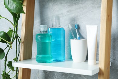 Photo of Bottles of mouthwash, toothbrushes and toothpaste on shelf in bathroom