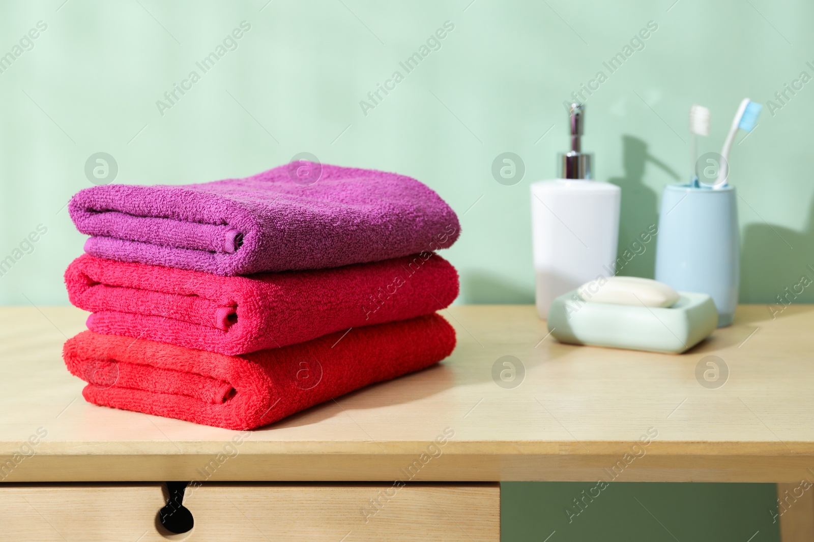 Photo of Fresh colorful terry towels and hygiene products on wooden table in bathroom, closeup