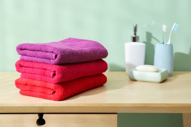 Photo of Fresh colorful terry towels and hygiene products on wooden table in bathroom, closeup