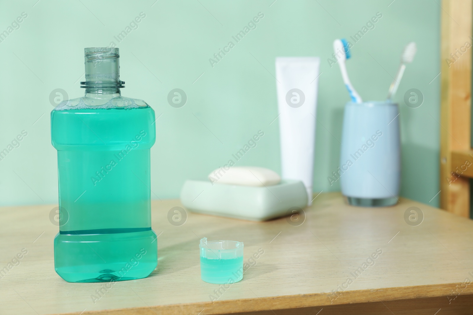 Photo of Bottle and cap of mouthwash on wooden shelf in bathroom