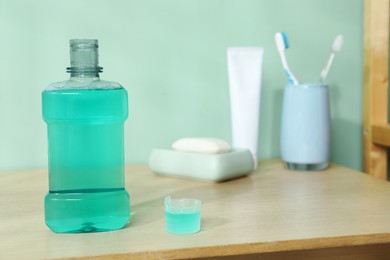 Photo of Bottle and cap of mouthwash on wooden shelf in bathroom