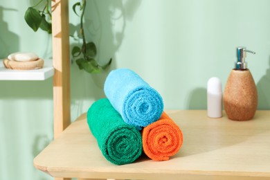 Photo of Fresh colorful terry towels and hygiene products on wooden table in bathroom