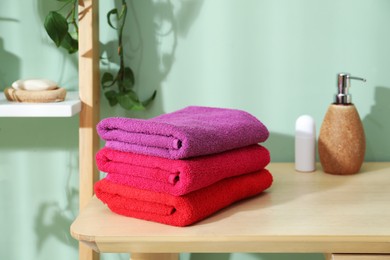 Photo of Fresh colorful terry towels and hygiene products on wooden table in bathroom