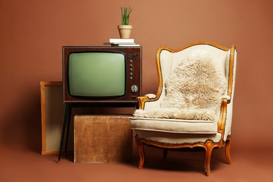 Photo of Retro TV set, armchair and other used stuff on brown background