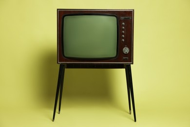 Photo of Retro TV set on stand against olive background. Used stuff
