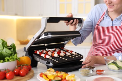 Photo of Woman cooking skewers with meat and vegetables on electric grill at home, closeup