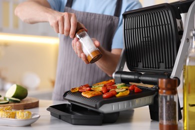 Photo of Man adding salt to vegetables cooking on electric grill in kitchen, closeup