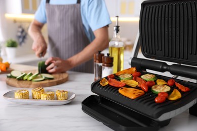 Photo of Man cutting zucchini while cooking vegetables on electric grill in kitchen, closeup
