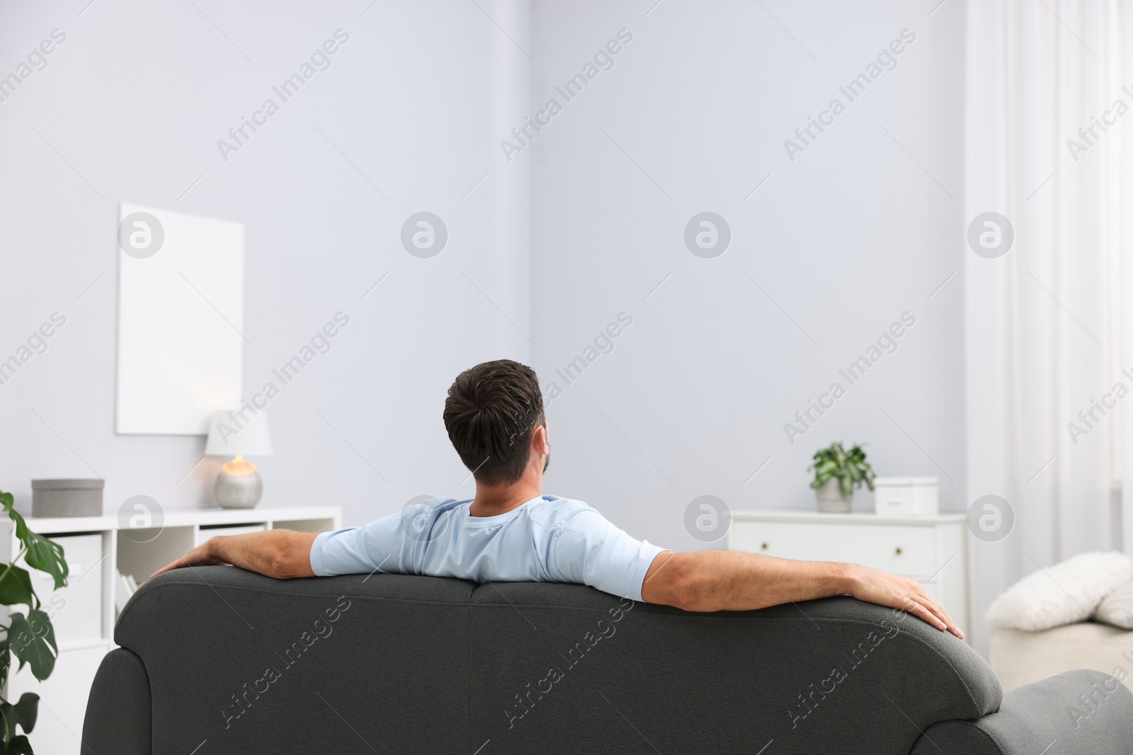 Photo of Happy man resting on sofa at home, back view